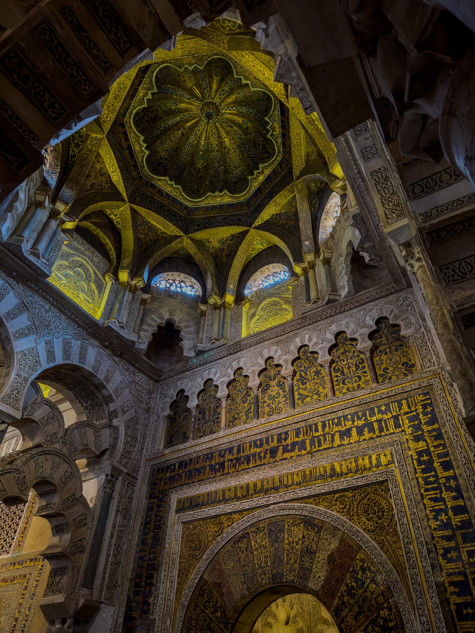 Artistic upwards photo of the interior of the Mosque of Cordoba, with dim lighting highlight the intricate sculpting and paint.