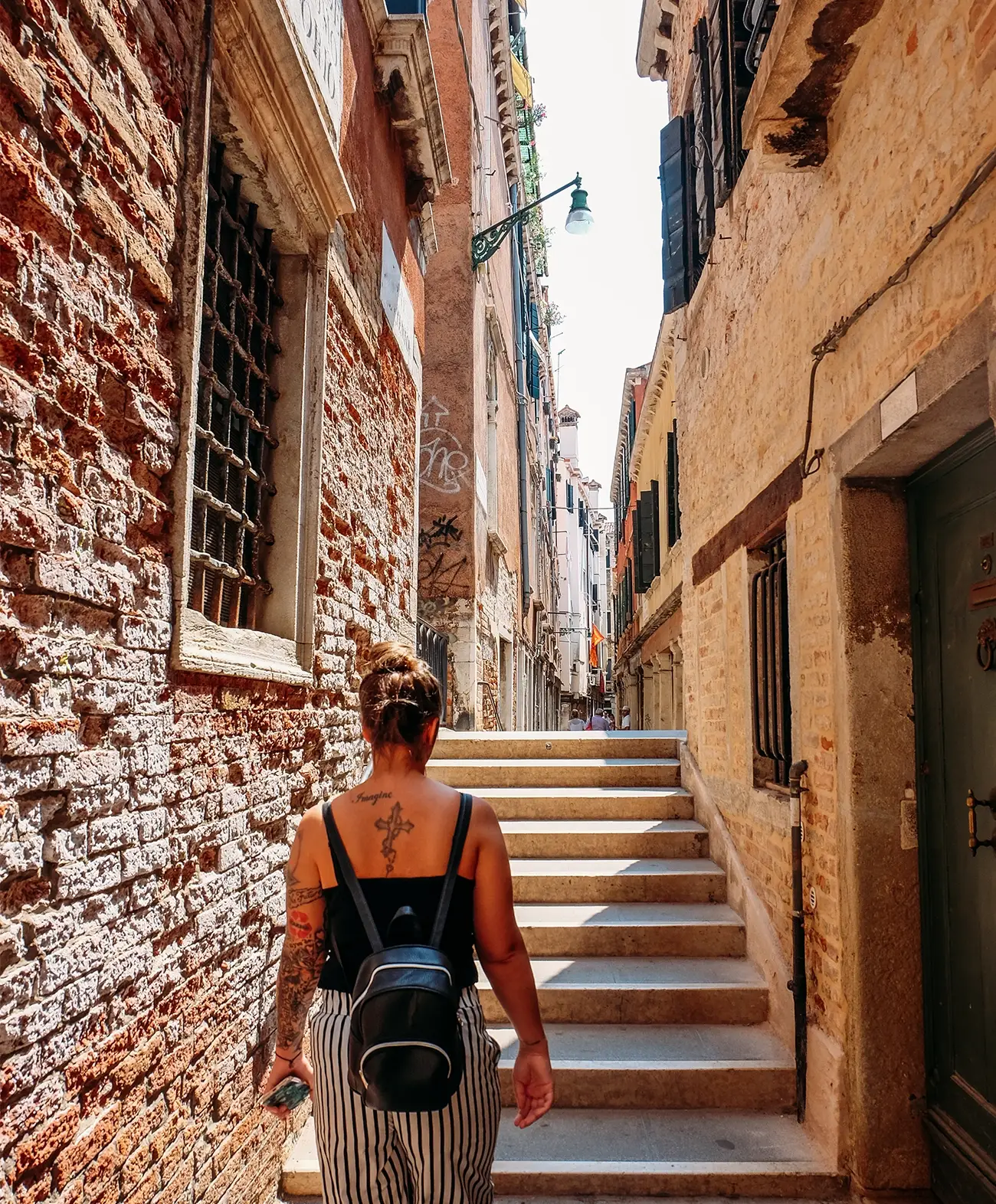 Young millennial woman with a tattoo walking up steps of an old city in Spain.